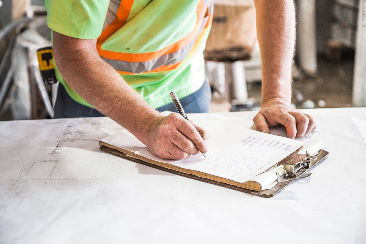 Technician inspecting an open septic tank and taking notes on a clipboard